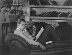 Actor Richard Arlen, Publicity Portrait Smoking Cigarette and Reading Script on Sofa, 1930's