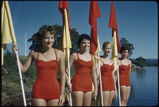 Four Young Adult Women Wearing Red One-Piece Bathing Suits and Holding Red and Yellow Flags, Australia, 1960