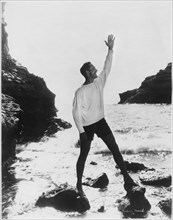 Actor Fredric March Standing with Raised Arm on Rocky Beach, California, USA, early 1940's