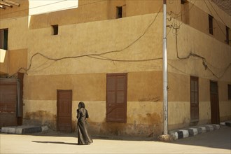 Muslim Woman with Camera Standing near Shuttered Building on Street Corner, Luxor, Egypt