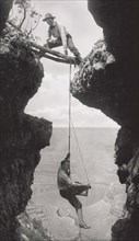 Photographer, Emery or Elsworth Kolb, Suspended on Climber's Rope in Crevasse and Photographing Canyon Wall as Another Man Straddles Cliff Opening while Holding the Rope, Grand Canyon, Arizona, USA, b...