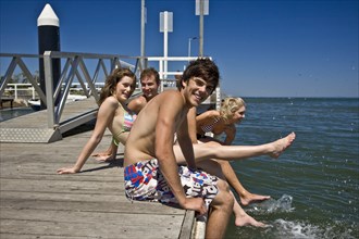 Two Smiling Young Couples Sitting on Edge of Pier