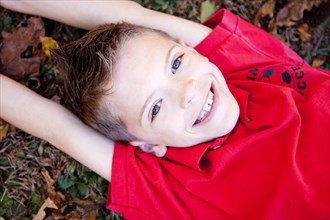 Smiling Boy With Arms Above Head Laying on Ground, High Angle View