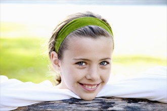Smiling Girl Wearing Green Headband with Chin Resting on Fence