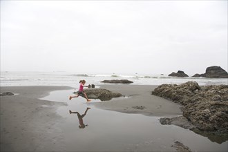 Girl Jumping Over Tidal Pool on Beach