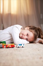 Smiling Girl Portrait on Floor with Toy Cars and Trucks