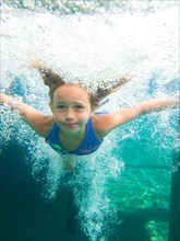 Young Girl Swimming Underwater in Pool Surrounded by Bubbles