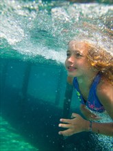 Young Girl Swimming Underwater in Pool Surrounded by Bubbles, Profile