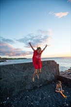 Young Girl Jumping off Lava Rock Wall while her Brother is Playing in  Black Sand at Ocean Beach, Hawaii, USA