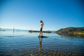Young Girl Standing on Rock Dipping her Toes into Shallow Water, Lake Tahoe, Nevada, USA