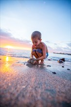 Young Boy Gathering Wet Sand at Beach at Sunset, Hawaii, USA