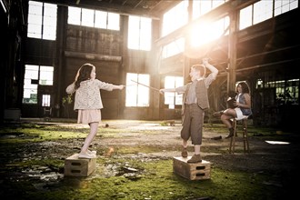 Two Children Play Fighting with Another Older Child Reading Book in Abandoned Warehouse