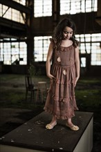 Young Girl Standing on Desk Looking Down in Abandoned Warehouse, Portrait