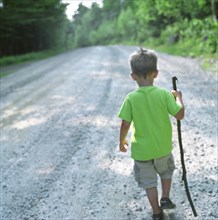 Young Boy with Stick Walking Down Path