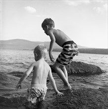 Two Young Boys Playing on Rock in Lake
