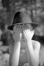 Young Boy Wearing Fedora Hat and Covering Face With Hands