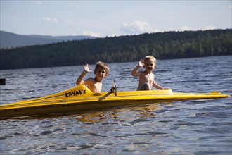 Two Young Boys Waving on Yellow Kayak on Lake