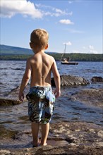 Young Boy in Bathing Suit Standing on Rocks at Water's Edge