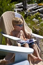 Young Boy in Sunglasses Sucking on Lollipop in Adirondack Chair