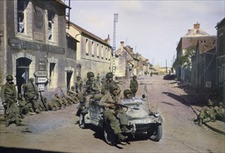 American Paratroopers in Captured German Jeep Patrolling Carentan while other American Soldiers Rest against a Building, Normandy, France, June 1944