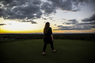 Rear View of Mid-Adult Woman on Hilltop at Sunset