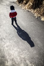 Rear View of Young Boy with Long Shadow Walking down Path,