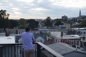 Rear View Portrait of Teenage Boy on Roof Deck Looking at View of Town