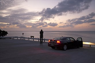 Rear View of Man near Parked Car Looking out to Sea at Sunset