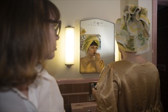 Woman Looking at another Woman Applying Lipstick in Bathroom Mirror