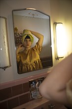 Young Adult Woman, Hair Wrapped in Towel, Looking in Bathroom Mirror