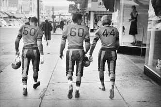Rear View of Three High School Football Players in Uniforms walking down Street