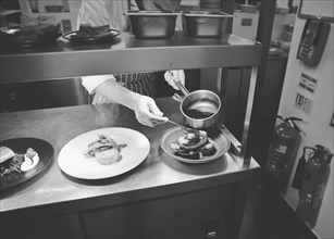 Chef pouring Sauce over Food in Restaurant Kitchen