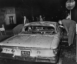 Detective examining burned out Police Car after night of rioting due to fatal shooting of Teen James Powell by Police Officer Lt. Thomas Gilligan, Herkimer Street and Nostrand Avenue, July 1964