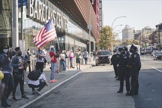 Man holding up American Flag at Barclays Center, opposite a Line of Police during Celebration of President-Elect Joe Biden
