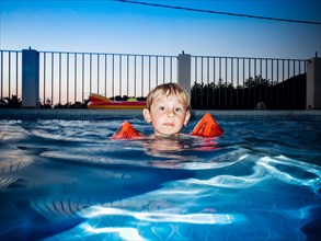 Young Boy floating in Swimming Pool at Sunset,