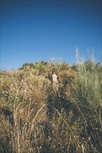 Rear View of Shirtless boy climbing Hill through Thick Foliage,