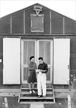 Mr. and Mrs. Hirata reading Letter while standing on wooden stairs in front of YMCA building