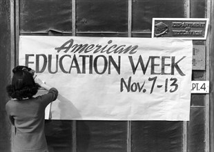 Woman hanging Sign promoting American Education Week to Wall of Education Department office