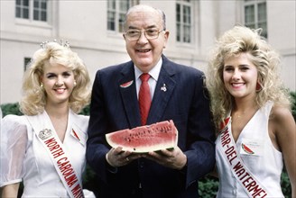 North Carolina Jesse Helms holding watermelon and standing between two beauty pageant winners at event sponsored by the National Watermelon Association