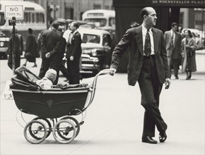 Man standing on Sidewalk with one hand on baby carriage