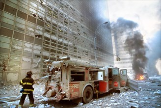 New York City fire fighter pulling water hose from fire truck amid debris and burning buildings following September 11th terrorist attack on World Trade Center