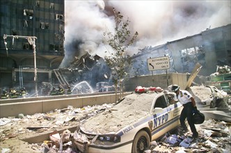 Rescue worker reaching into a New York Police car covered with debris with smoldering ruins in background