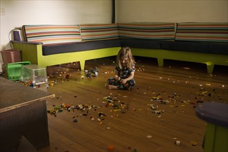 Young Boy sitting on Floor of Large Room surrounded by Plastic Toy Pieces