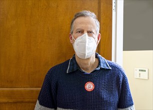 Man wearing Protective Face Mask with COVID-19 vaccination sticker on sweater