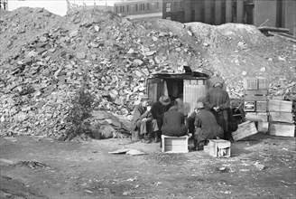 Unemployed Workers in front of Shack next to pile of rubble
