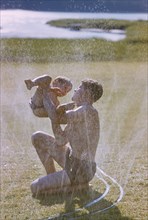 Father and Son Playing near Water Sprinklers