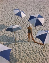 Rear View Portrait of Woman in One-Piece Swimsuit surrounded by Umbrellas on Beach
