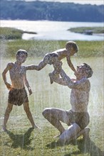 Father playing with Two Sons near Water Sprinklers