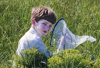Young Boy sitting in Grassy Field with Butterfly Net