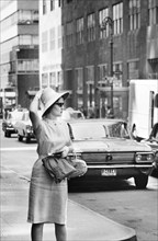 Woman on Street Corner holding Hat on Head